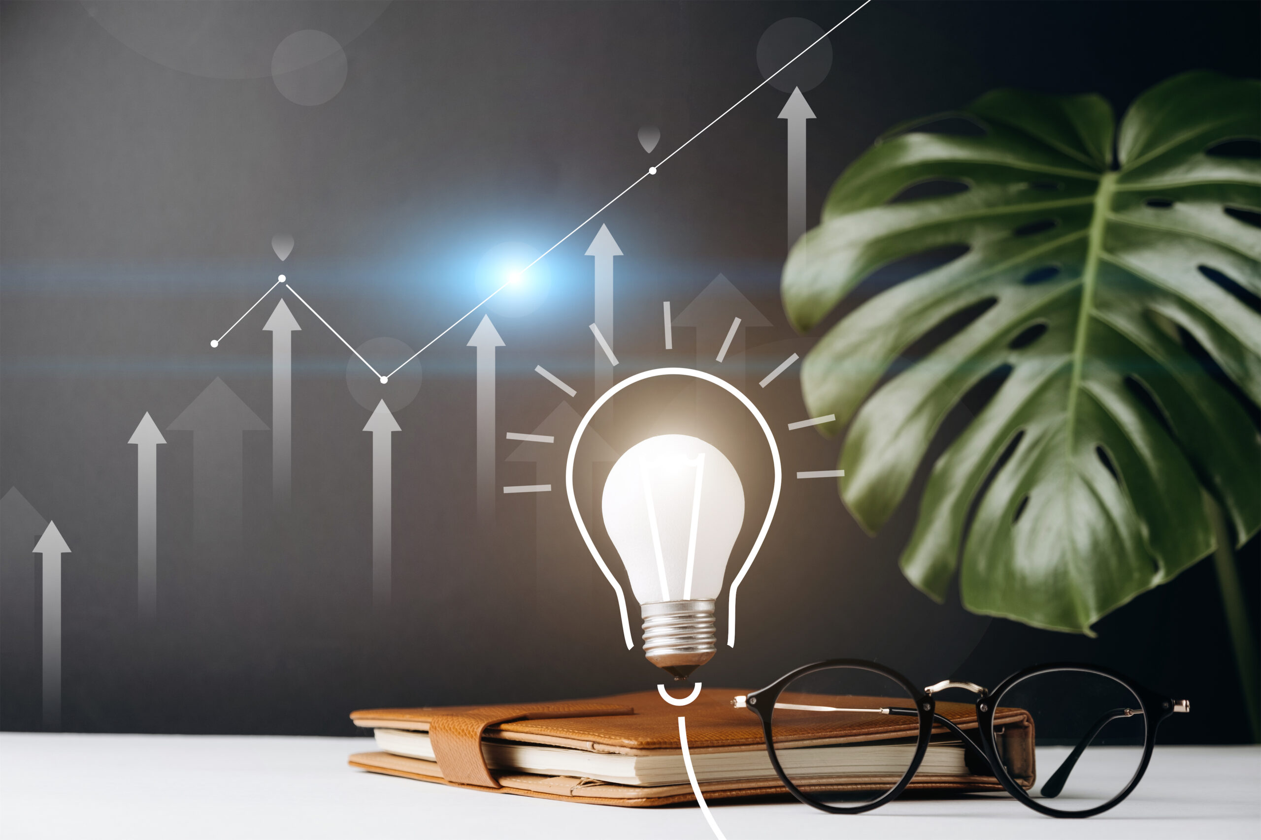 Home office desk table workspace with a notebook, light bulb with innovative technology and creativity, pen, cup coffee, monstera leaves and eyeglasses on grey background. Copy space mockup template